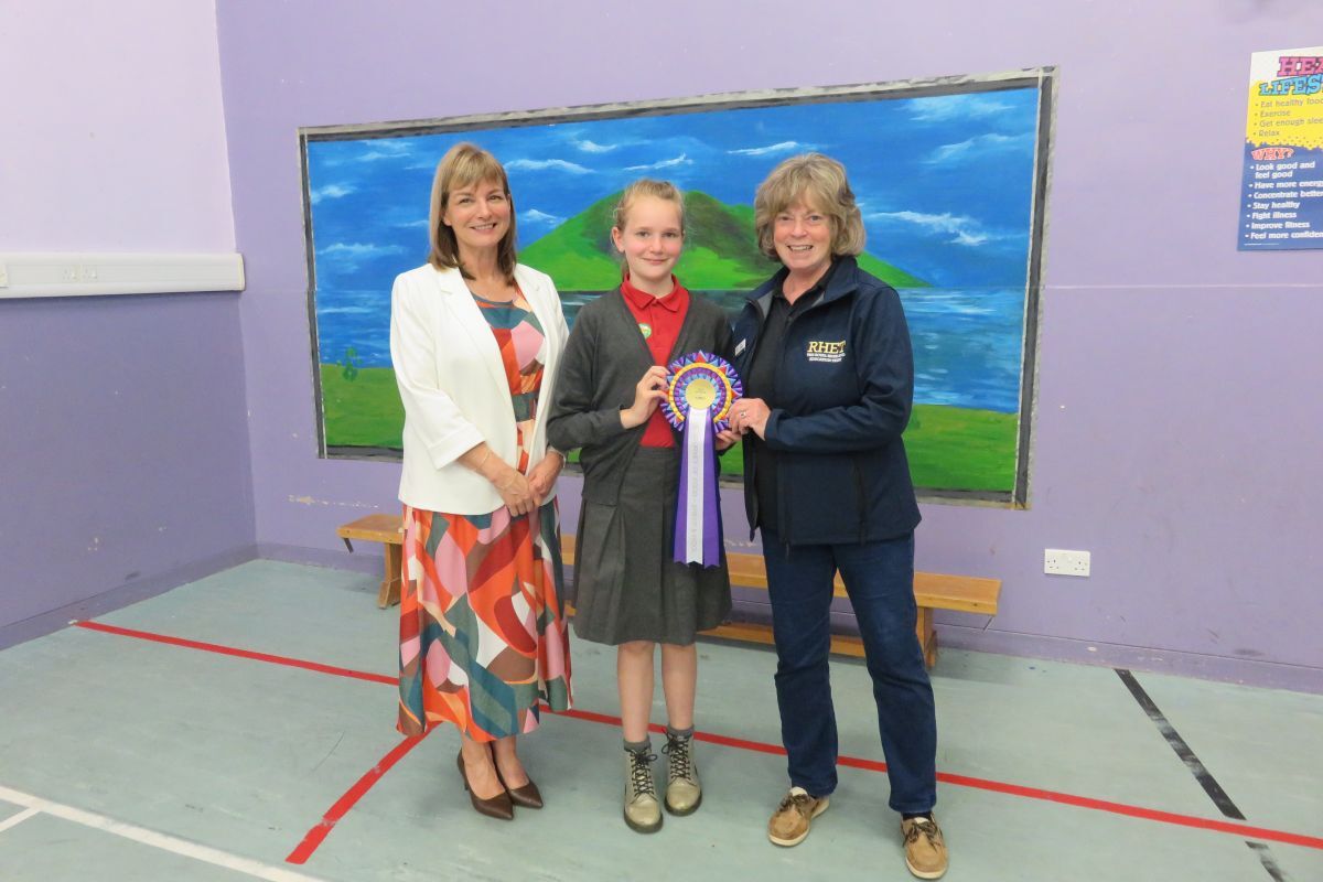 Jane Cameron of Ayrshire and Arran Royal Highland Education Trust presents Connie McKie with a copy of her winning rosette while head teacher Susan Foster proudly looks on. Photograph: Lamlash Primary.