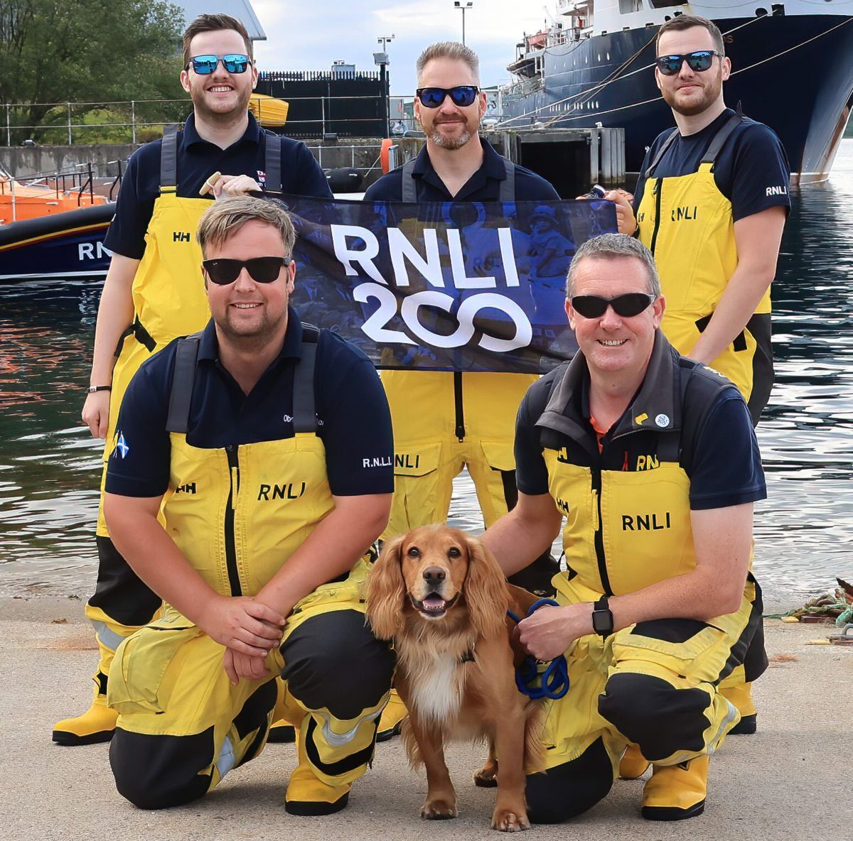 Marking the moment with Flynn the station dog were mechanic Tom Kennedy, coxswain Ally Cerexhe, and crew members at the back Cameron Scott, Gillies Pagan and Andrew Scott. Photograph: Stephen Lawson/RNLI