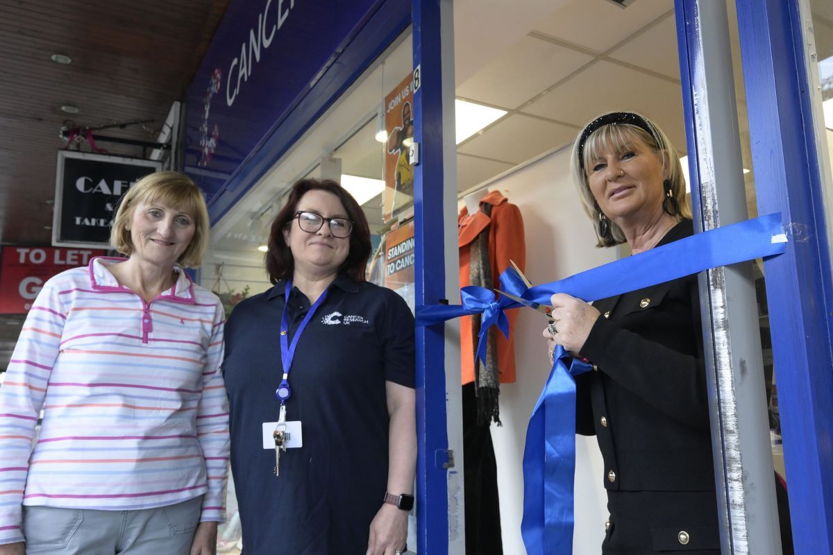 Paula MacAskill cuts the ribbon at the Cancer Research Shop in Fort William HIgh Street to welcome new Manager MIchele Collins (centre) watched by volunteer Margaret Conaghan. Photograph: Iain Ferguson, alba.photos.