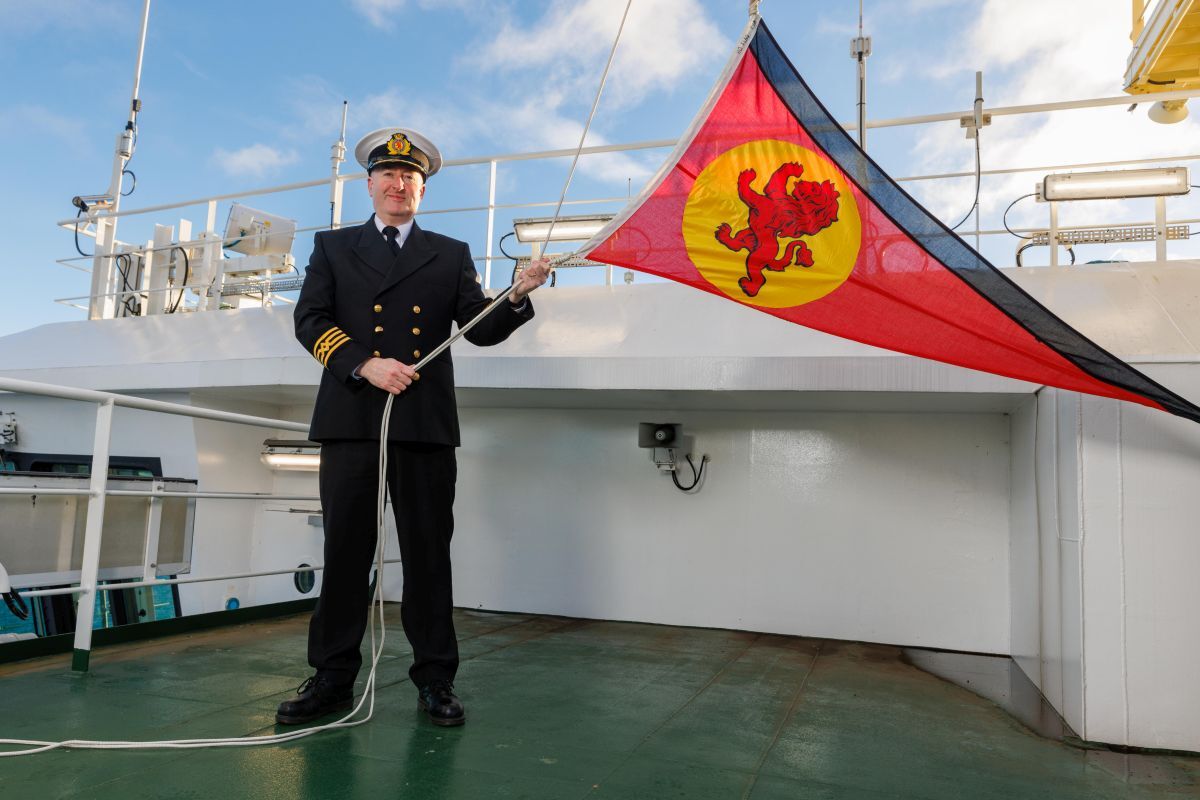 Master of MV Glen Sannox Michael Mackinnon raises CalMac's red ensign on the ship to signify its new operator. Photograph: Clark Communications.