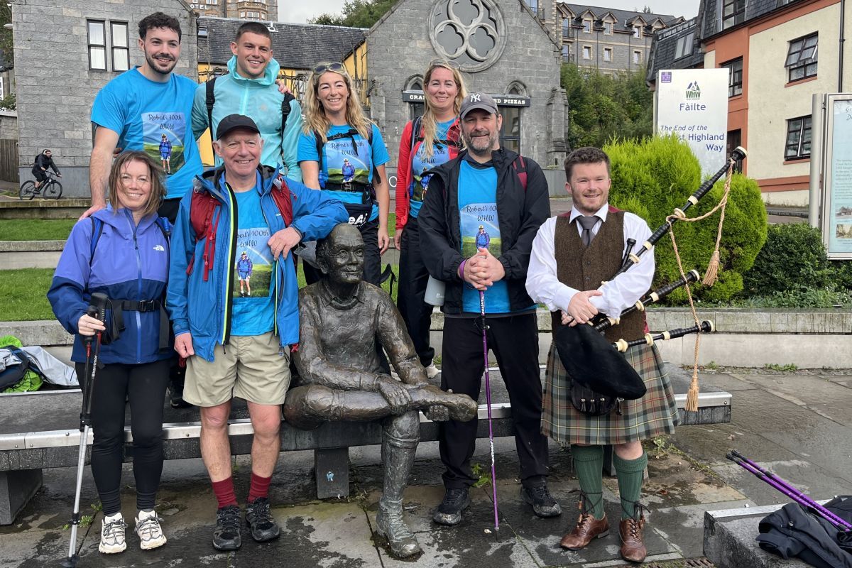 Robert Marshall at the &lsquo;Man with Sore Feet&rsquo; statue at the end of the West Highland Way at Fort William with his six children and The Munro Bagpiper, who piped them across the finish line.