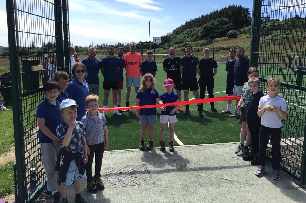 Primary pupils Maisie and Ezme officially open Gigha’s new multi-use games area, joined by fellow Gigha Primary School pupils, with the island’s farmers and fish farmers, and members of the community, behind. Photograph: Gigha Primary School.