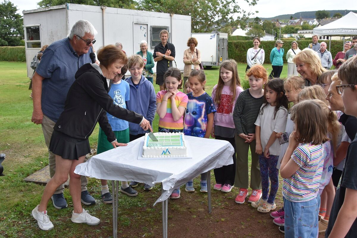 Young tennis players watch eagerly as Maggie Carson cuts the cake. Young tennis players watch eagerly as Maggie Carson cuts the cake.