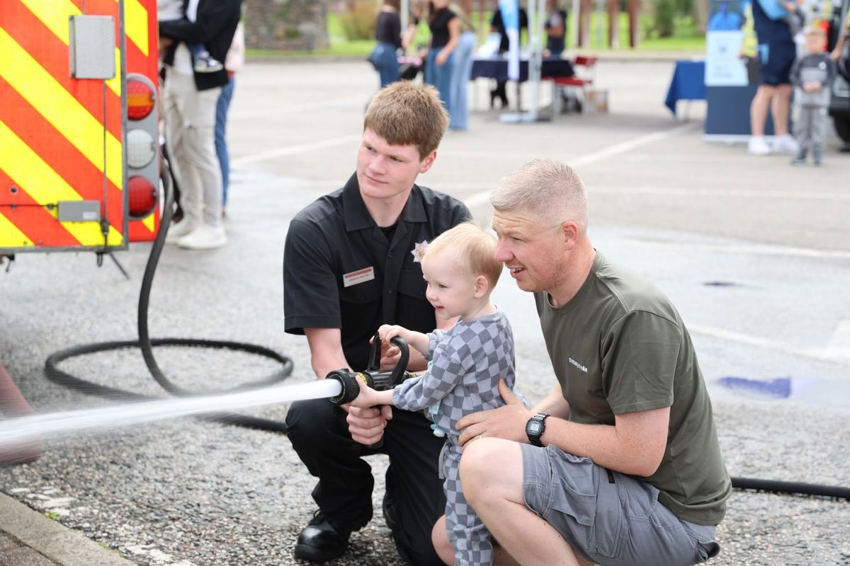Little Luke Willis tries the fire hose with the help of his dad John, right, and firefighter Andrew Brodie. Photograph: Kenny Craig.